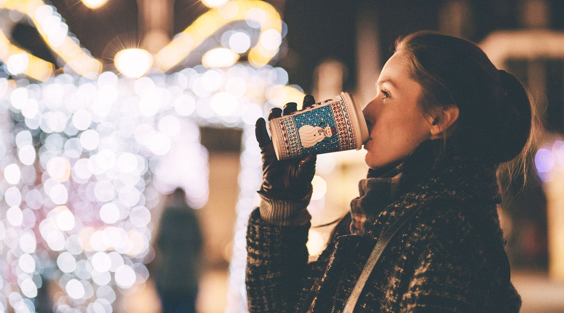 Woman drinking warm holiday drink looking at lights