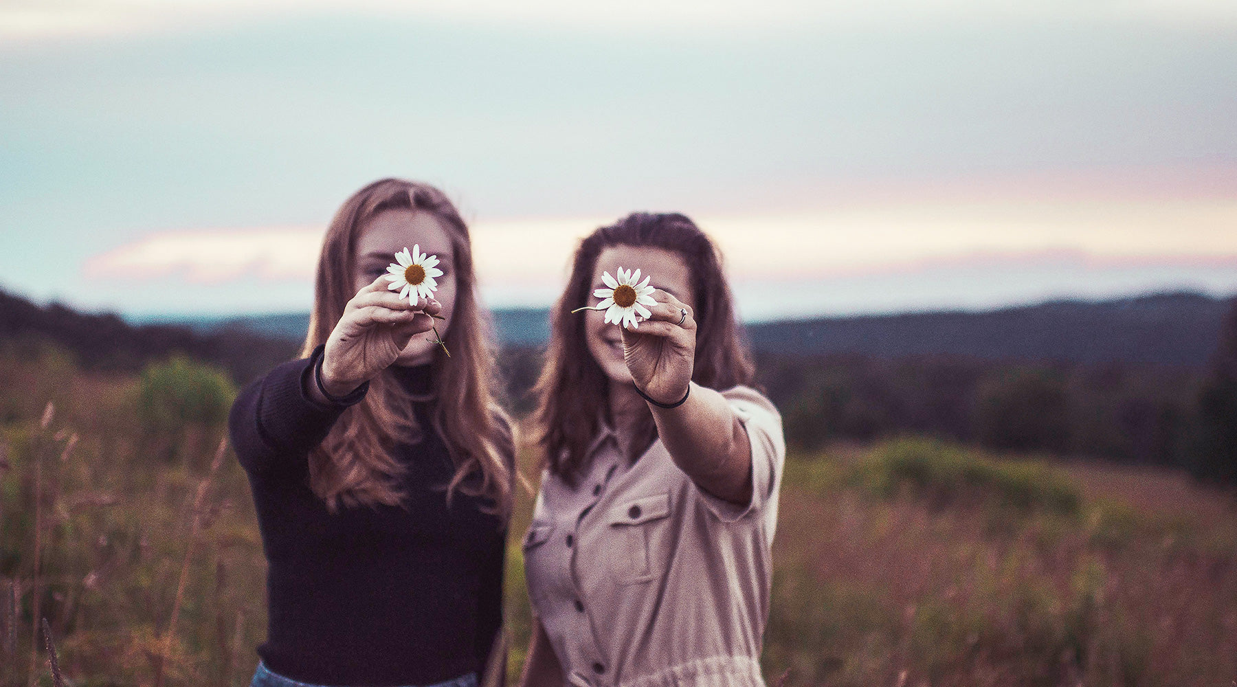 Two girls holding daisies in front of faces